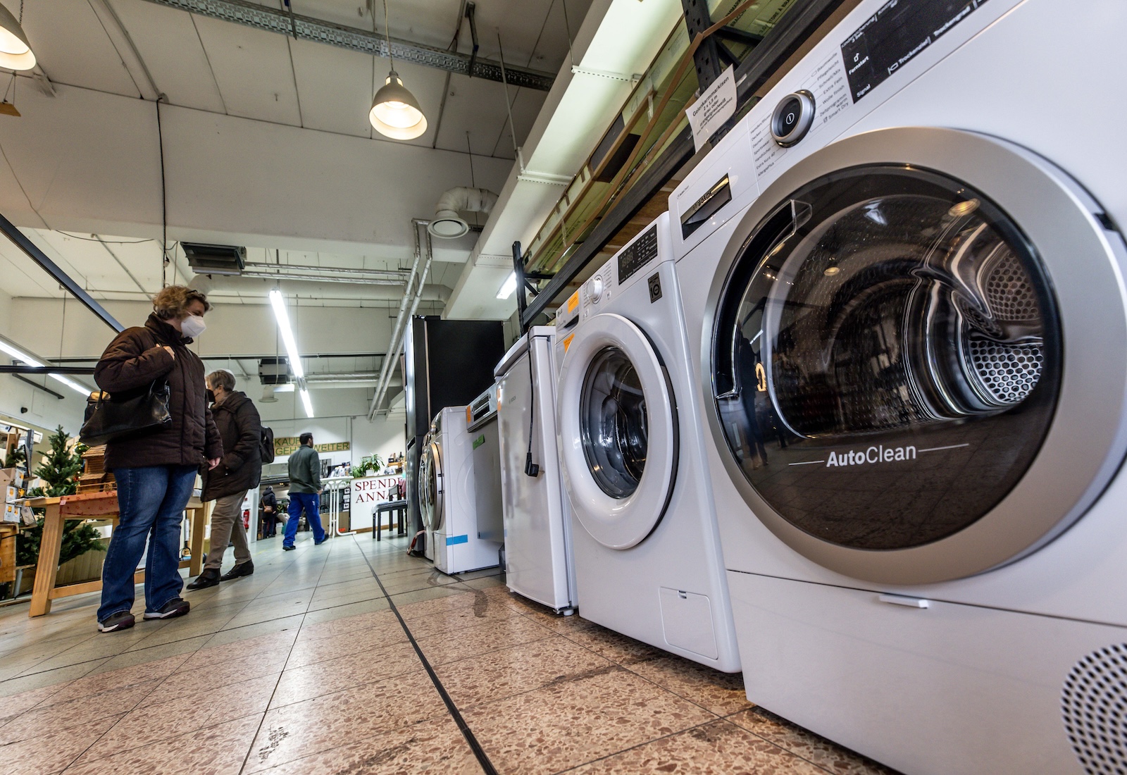 White washing machines were lined up on the showroom floor, customers looking at them.