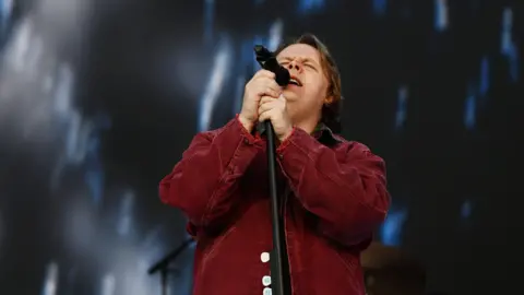 Lewis Capaldi performs on Radio 1's Big Weekend 2023 - singing into a microphone and wearing a red shirt.