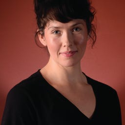 Allison Nichol Longtin stands in front of a red background in this headshot