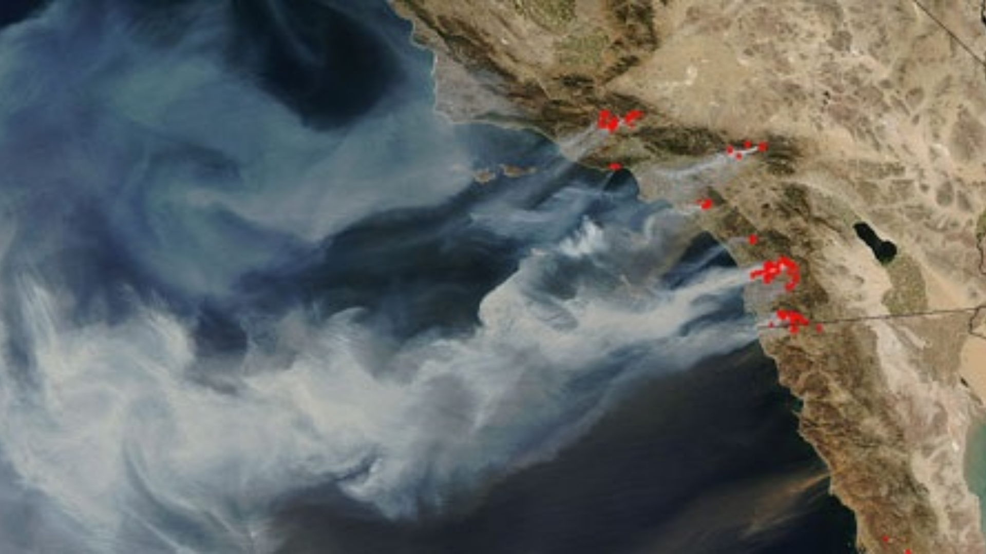 A view of the coastline from a satellite. White smoke rises from the coast.