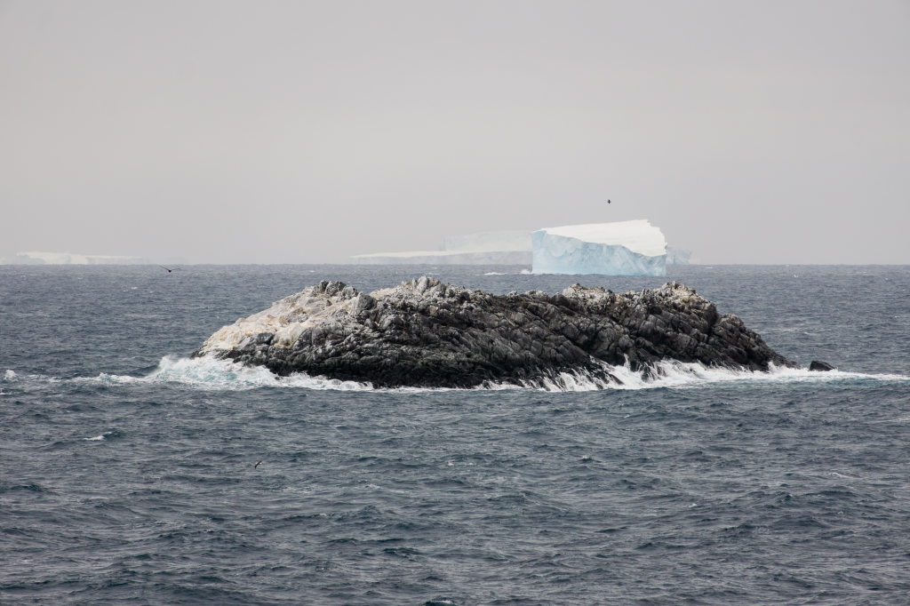 An uncharted island in the Weddell Sea with an iceberg in the distance.